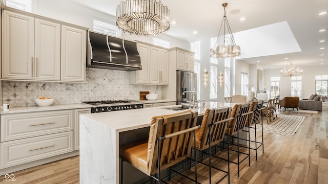 kitchen featuring sink, a chandelier, ventilation hood, hanging light fixtures, and an island with sink