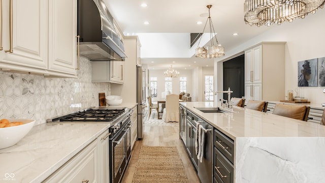 kitchen featuring sink, an inviting chandelier, hanging light fixtures, stainless steel appliances, and wall chimney range hood