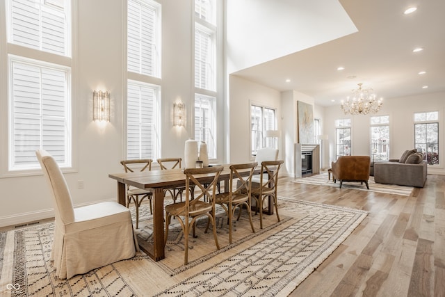 dining area with a towering ceiling, a notable chandelier, and light wood-type flooring