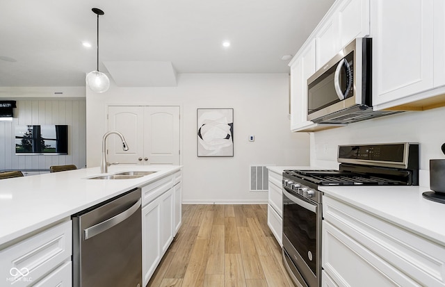 kitchen featuring sink, light hardwood / wood-style flooring, pendant lighting, stainless steel appliances, and white cabinets