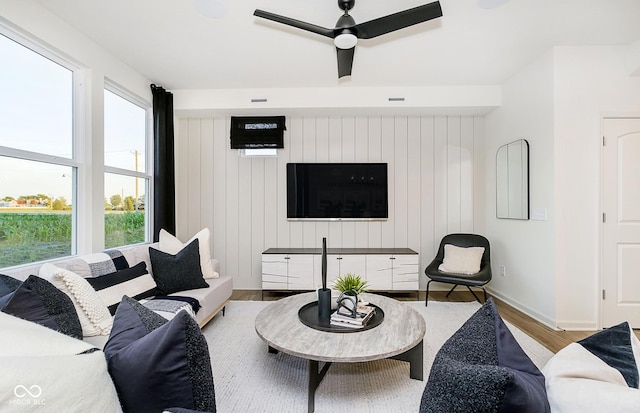 living room with ceiling fan, wood walls, a healthy amount of sunlight, and light wood-type flooring