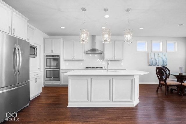 kitchen featuring appliances with stainless steel finishes, decorative light fixtures, a center island with sink, and wall chimney exhaust hood