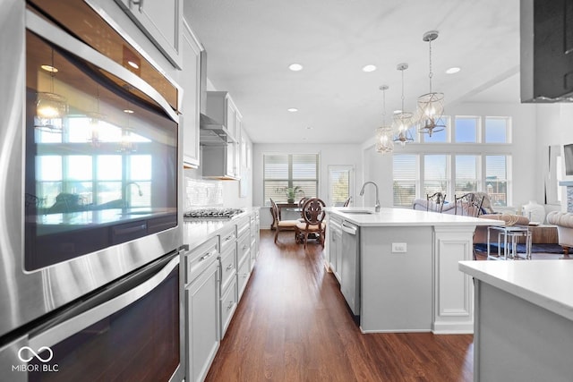 kitchen with appliances with stainless steel finishes, white cabinetry, sink, hanging light fixtures, and a center island with sink