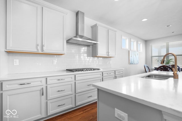 kitchen featuring wall chimney range hood, sink, dark wood-type flooring, backsplash, and stainless steel gas stovetop