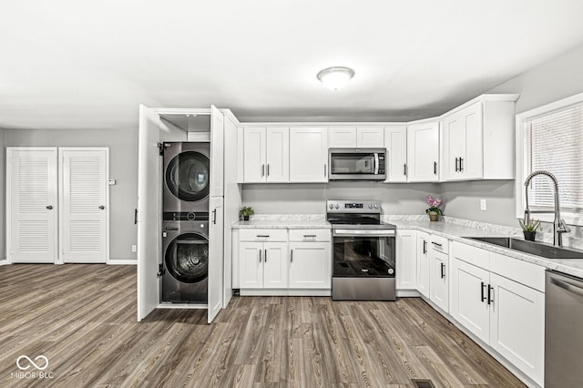 kitchen featuring sink, stainless steel appliances, white cabinets, and stacked washing maching and dryer