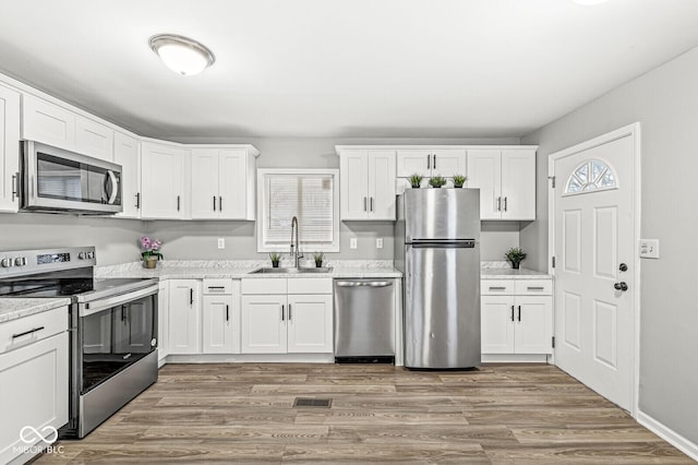 kitchen with sink, light hardwood / wood-style flooring, stainless steel appliances, light stone countertops, and white cabinets