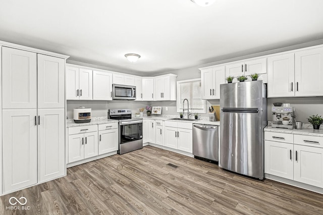 kitchen featuring appliances with stainless steel finishes, sink, white cabinets, light stone counters, and light hardwood / wood-style flooring