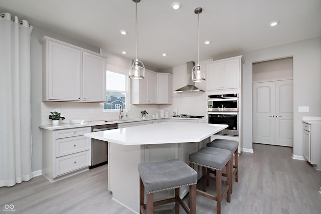 kitchen featuring wall chimney exhaust hood, white cabinetry, appliances with stainless steel finishes, a kitchen island, and pendant lighting