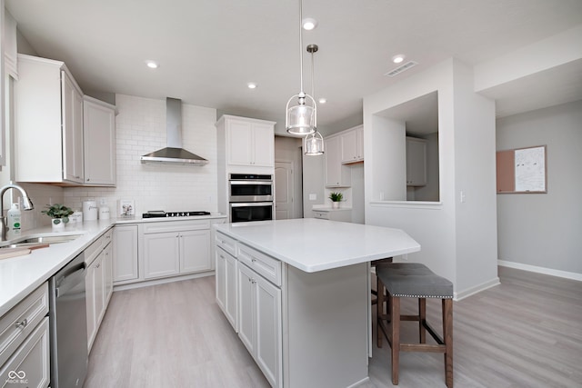 kitchen with appliances with stainless steel finishes, white cabinetry, sink, a center island, and wall chimney range hood