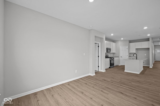 kitchen with white cabinetry, a kitchen island with sink, stainless steel appliances, light hardwood / wood-style flooring, and sink