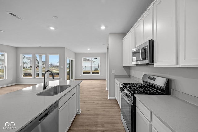 kitchen with appliances with stainless steel finishes, sink, white cabinetry, and light hardwood / wood-style floors