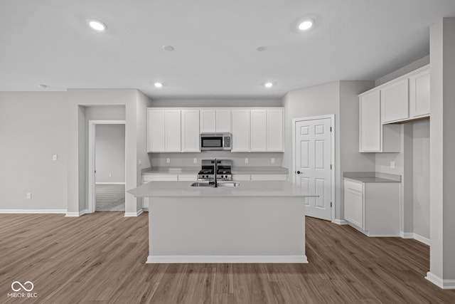 kitchen featuring appliances with stainless steel finishes, hardwood / wood-style flooring, white cabinetry, and a center island with sink