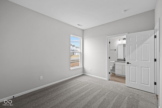 unfurnished bedroom featuring light carpet and connected bathroom