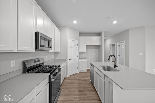 kitchen with a kitchen island with sink, light hardwood / wood-style floors, sink, appliances with stainless steel finishes, and white cabinets