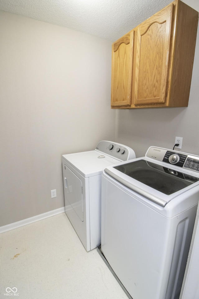 washroom featuring cabinets, washing machine and dryer, and a textured ceiling