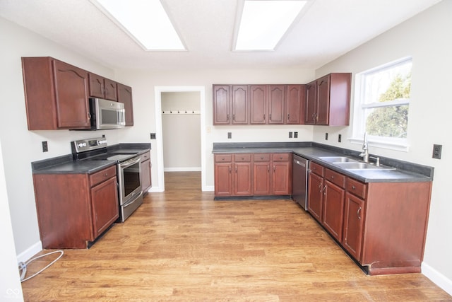 kitchen with appliances with stainless steel finishes, sink, light wood-type flooring, and a skylight