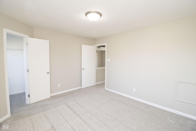 unfurnished bedroom with a walk in closet, light carpet, a textured ceiling, and a closet