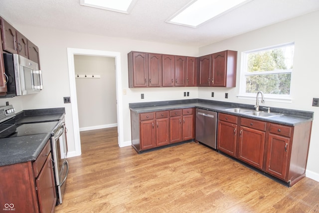 kitchen with sink, a skylight, light hardwood / wood-style flooring, a textured ceiling, and appliances with stainless steel finishes