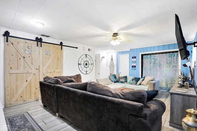 living room featuring a barn door, ceiling fan, and light hardwood / wood-style flooring