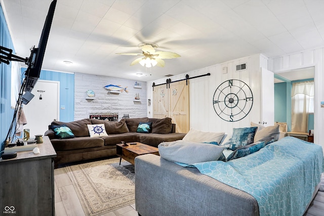 living room featuring ceiling fan, a barn door, and light hardwood / wood-style flooring