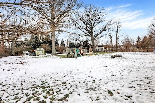 snowy yard with a playground and a storage shed