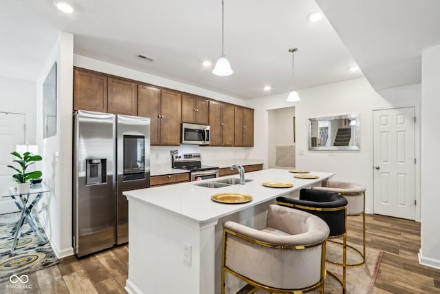 kitchen featuring pendant lighting, sink, appliances with stainless steel finishes, dark hardwood / wood-style floors, and a center island with sink