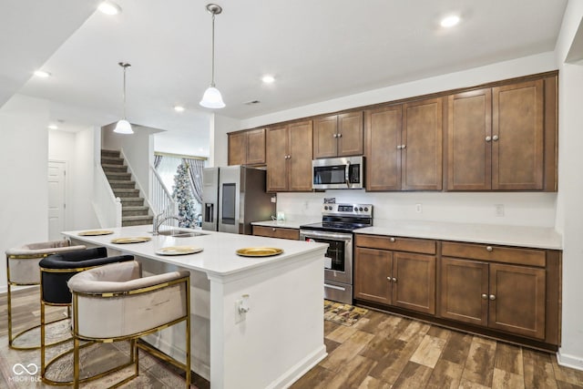 kitchen featuring pendant lighting, a breakfast bar, appliances with stainless steel finishes, dark hardwood / wood-style floors, and an island with sink