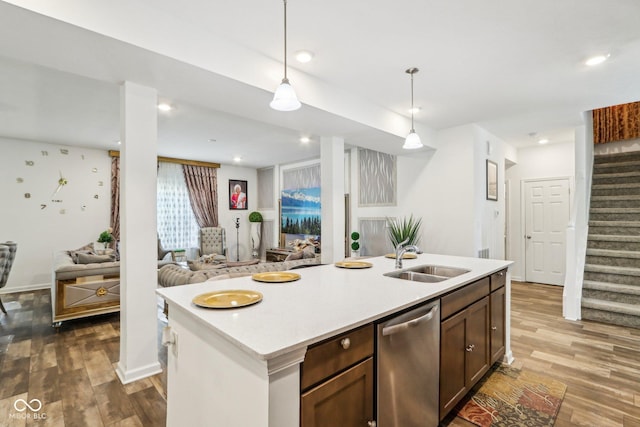 kitchen with decorative light fixtures, dishwasher, sink, hardwood / wood-style flooring, and a center island with sink