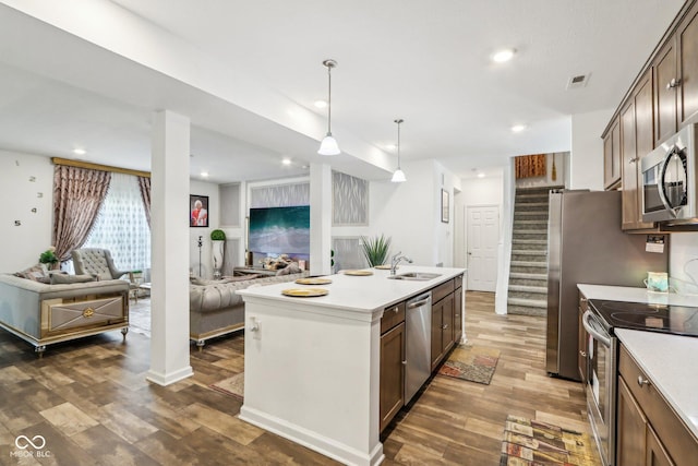 kitchen with dark wood-type flooring, sink, decorative light fixtures, appliances with stainless steel finishes, and a kitchen island with sink