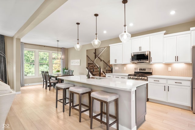 kitchen featuring appliances with stainless steel finishes, pendant lighting, white cabinetry, an island with sink, and sink