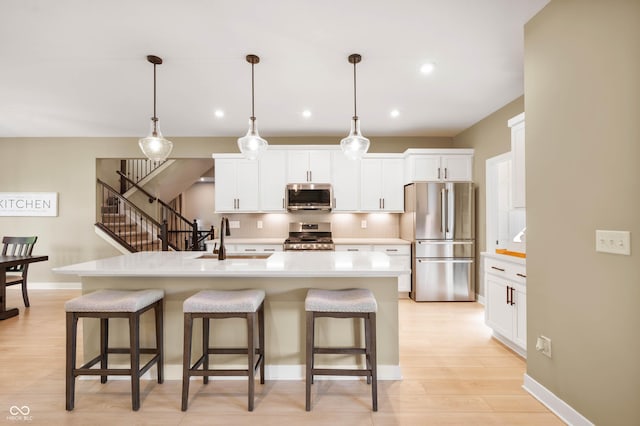 kitchen with a kitchen island with sink, sink, pendant lighting, and stainless steel appliances