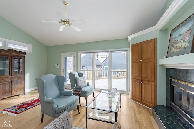 living area featuring vaulted ceiling, ceiling fan, light hardwood / wood-style floors, and a tile fireplace