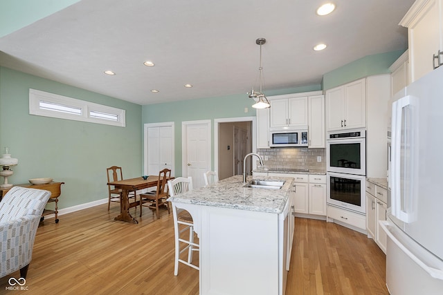 kitchen with sink, decorative light fixtures, a center island with sink, white appliances, and white cabinets