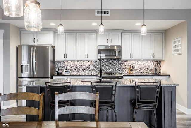 kitchen featuring appliances with stainless steel finishes, decorative light fixtures, a breakfast bar area, and dark stone countertops