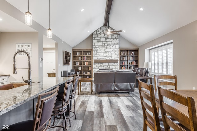 dining space featuring a fireplace, sink, vaulted ceiling with beams, dark hardwood / wood-style flooring, and ceiling fan