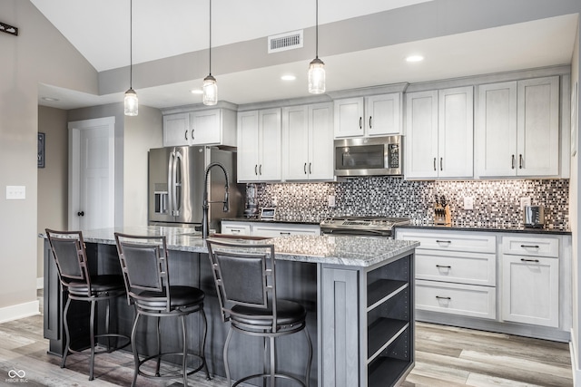 kitchen with pendant lighting, appliances with stainless steel finishes, a center island with sink, and dark stone counters