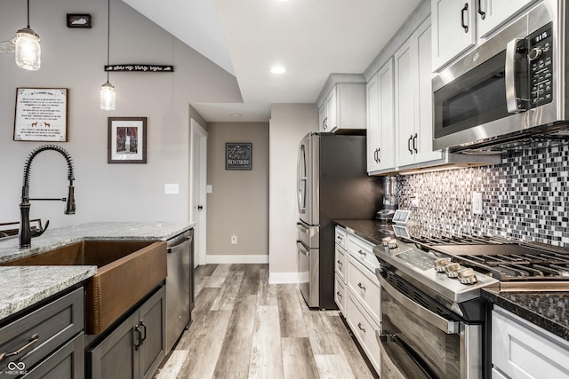 kitchen with dark stone countertops, white cabinets, hanging light fixtures, stainless steel appliances, and light wood-type flooring