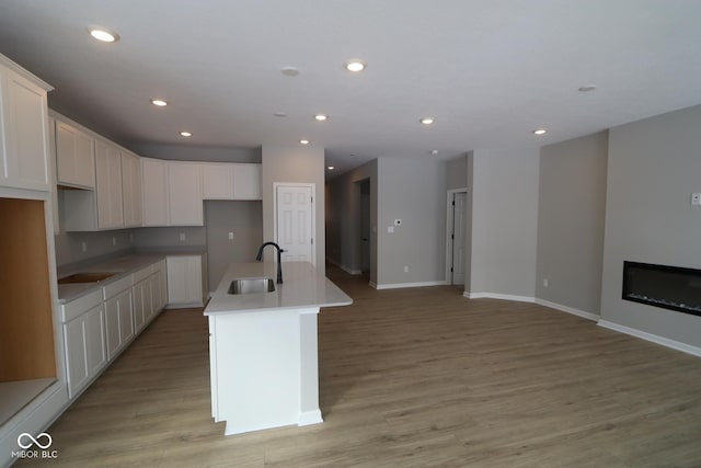 kitchen with white cabinetry, sink, light wood-type flooring, and a center island with sink