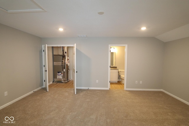 unfurnished bedroom with lofted ceiling, light carpet, and ensuite bath