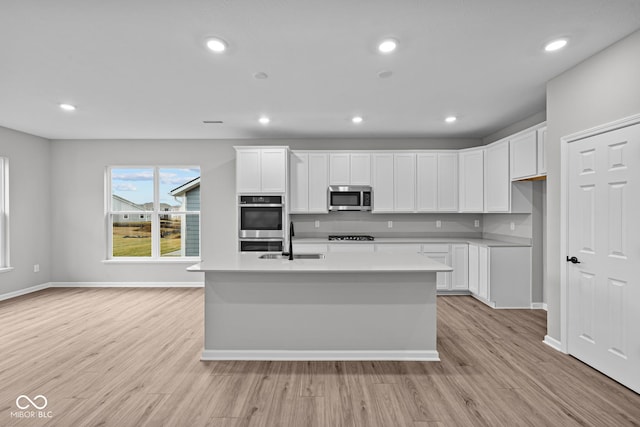 kitchen with white cabinetry, a center island with sink, light wood-type flooring, sink, and appliances with stainless steel finishes