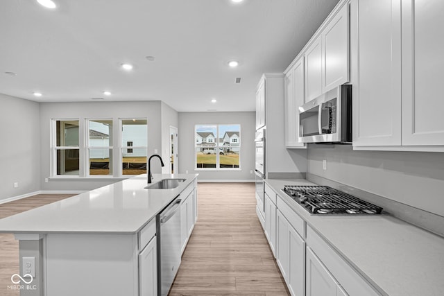 kitchen featuring appliances with stainless steel finishes, light hardwood / wood-style floors, sink, white cabinetry, and a kitchen island with sink