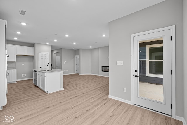 kitchen featuring white cabinetry, light wood-type flooring, a kitchen island with sink, sink, and dishwasher