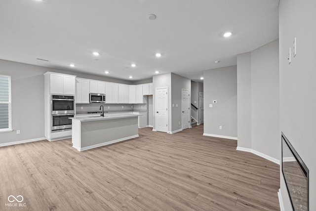 kitchen with light hardwood / wood-style flooring, appliances with stainless steel finishes, sink, white cabinets, and a kitchen island with sink