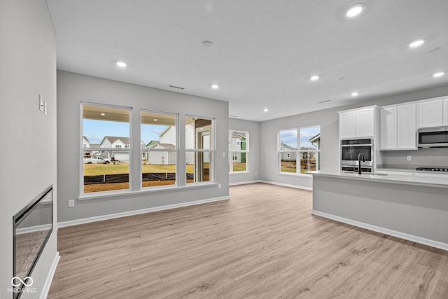 kitchen with sink, light hardwood / wood-style floors, white cabinetry, and black gas stovetop