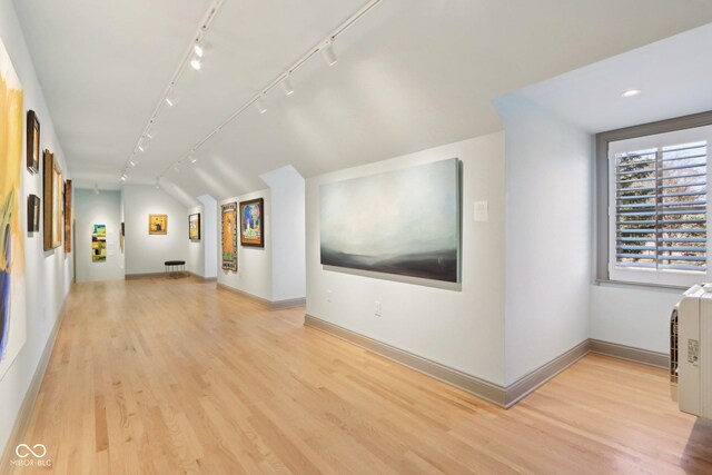 interior space with baseboards, lofted ceiling, light wood-style floors, and track lighting