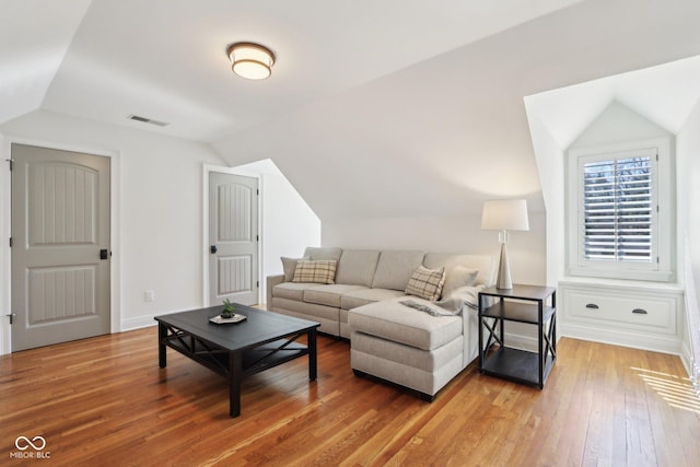 living room featuring visible vents, baseboards, light wood-style flooring, and vaulted ceiling