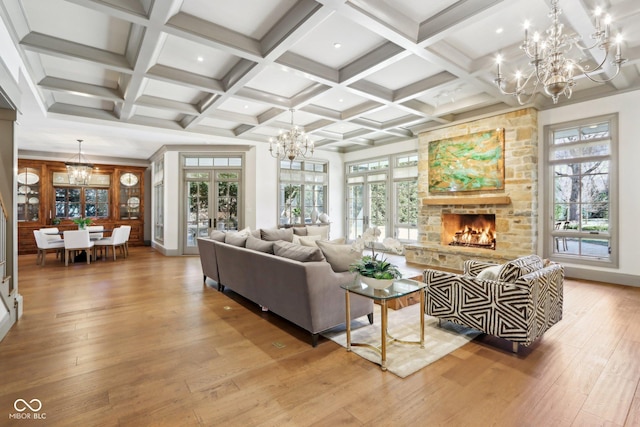 living room featuring beamed ceiling, a stone fireplace, a chandelier, and hardwood / wood-style flooring