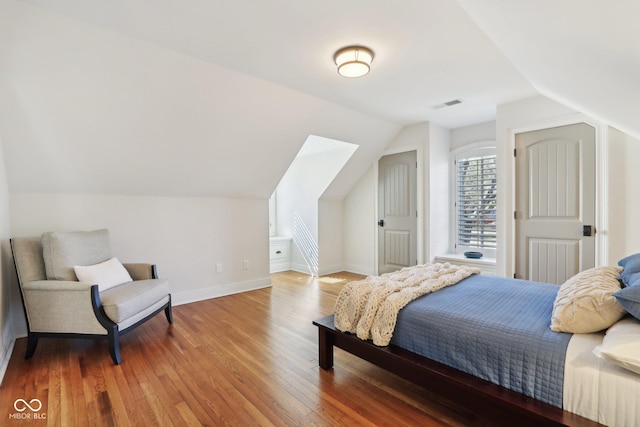 bedroom with vaulted ceiling, visible vents, baseboards, and wood finished floors