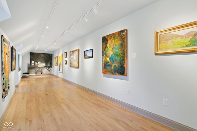 corridor featuring track lighting, wood finished floors, and baseboards