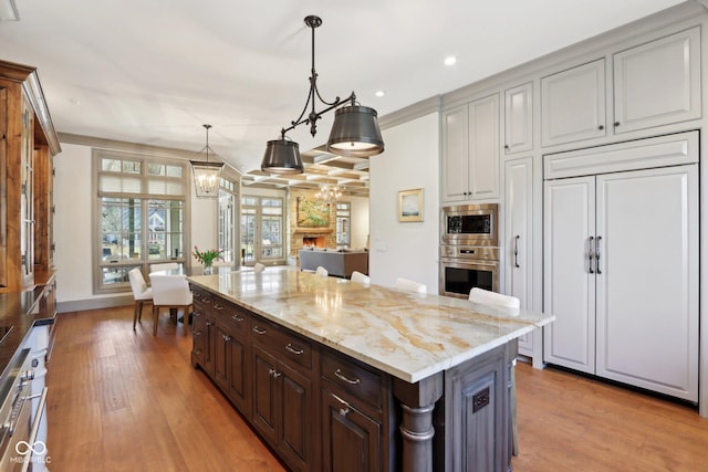 kitchen with light wood finished floors, light stone countertops, built in appliances, and a chandelier